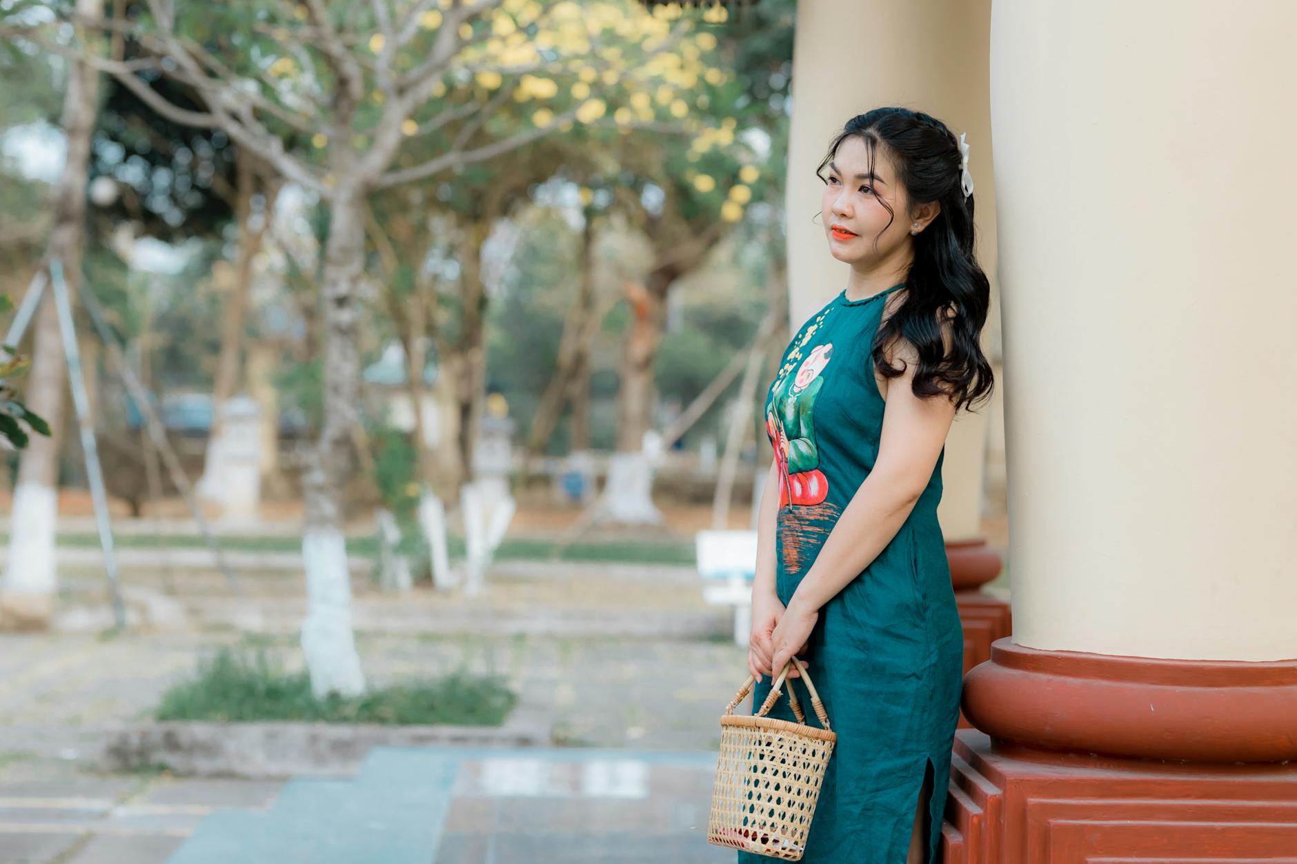 Kobieta w zielonej sukience ołówkowej z wiklinowym koszykiem na dworze