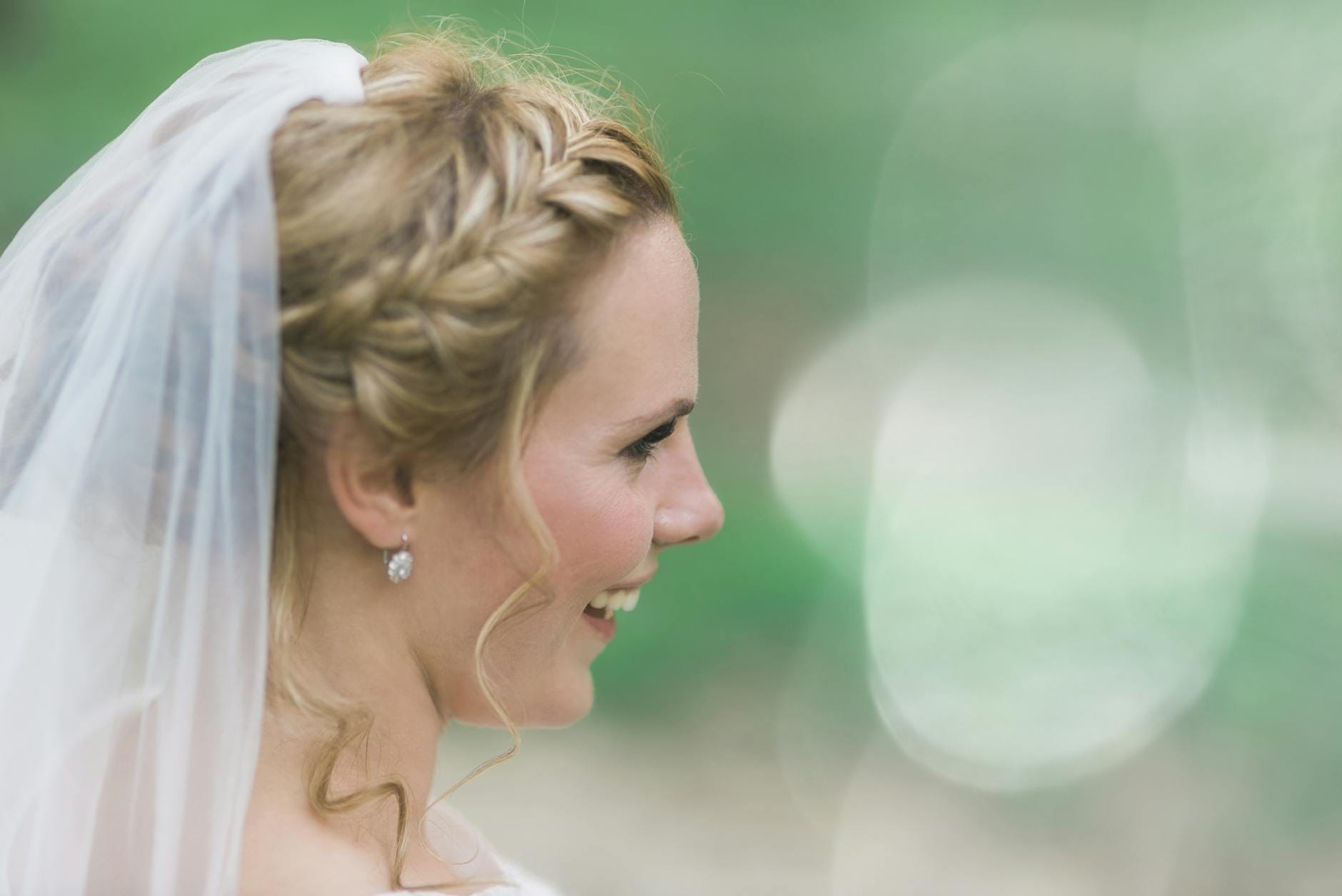 Panna młoda z warkoczem i welonem w zielonym plenerze, profil