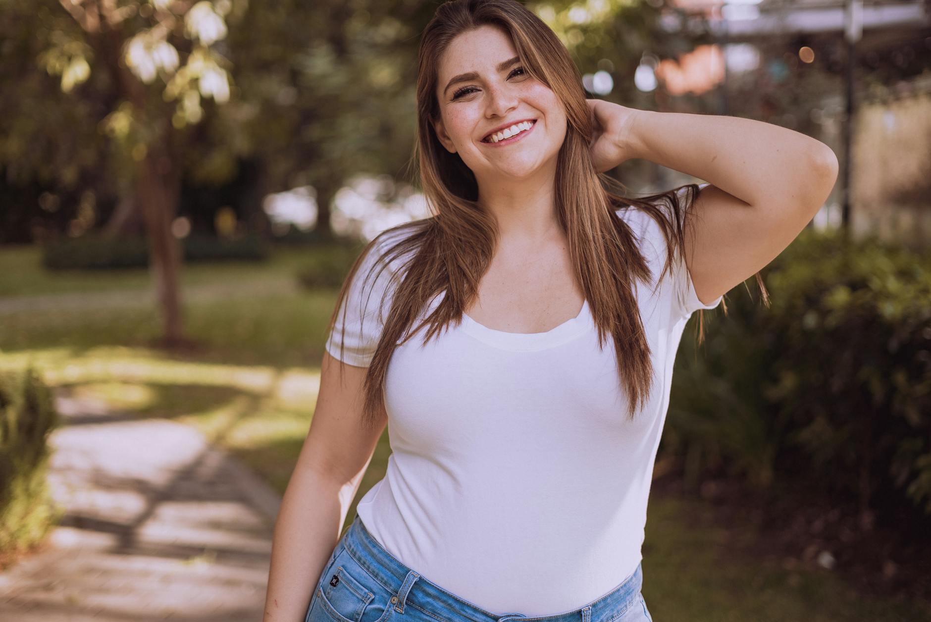 Uśmiechnięta kobieta w białej koszuli na zewnątrz, pewna swojego wyglądu