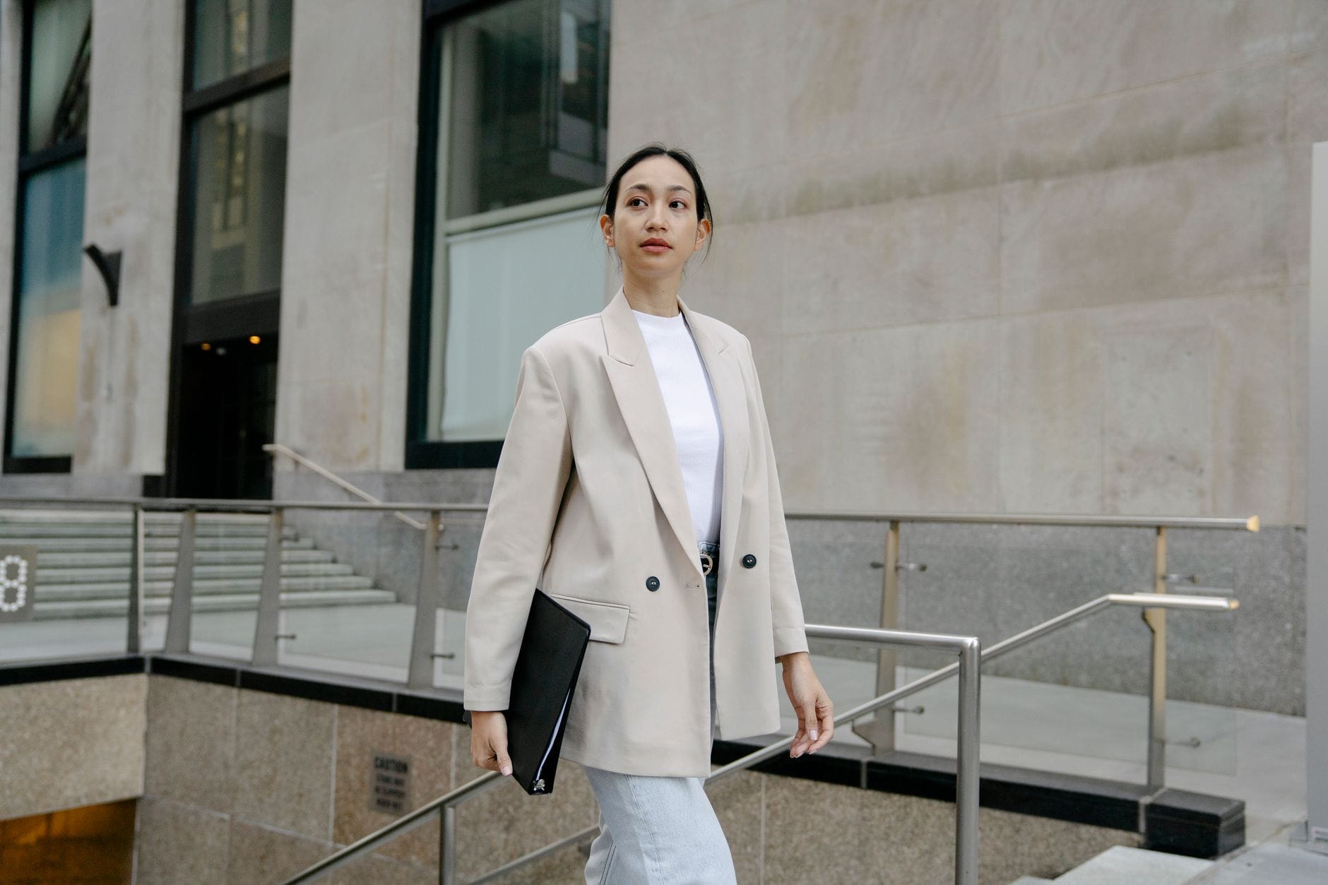 Elegancka Azjatka w marynarce idzie ulicą z teczką w ręku