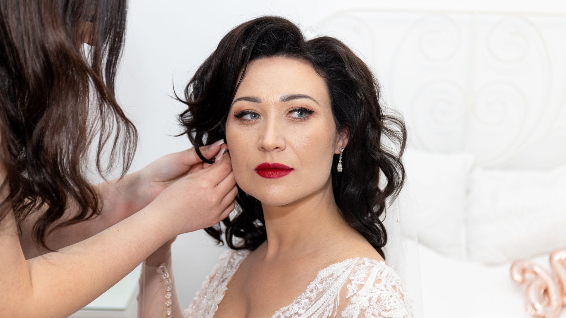 Panna młoda w upiętych włosach zakłada eleganckie kolczyki na wesele